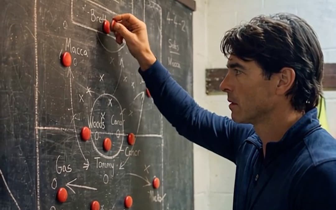 A coach pinning magnets to a chalkboard team sheet in a changing room